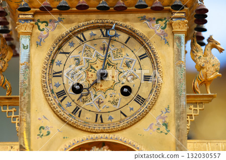 An ornate, gilded clock with Roman numerals and decorative patterns An ornate, gilded clock with Roman numerals and decorative patterns 132030557