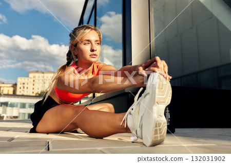 Athletic woman stretches on urban rooftop in bright sun during fitness routine 132031902