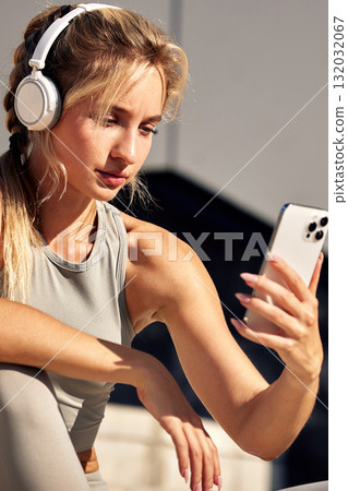 Woman wearing headphones takes a selfie with her phone during an outdoor workout session 132032067