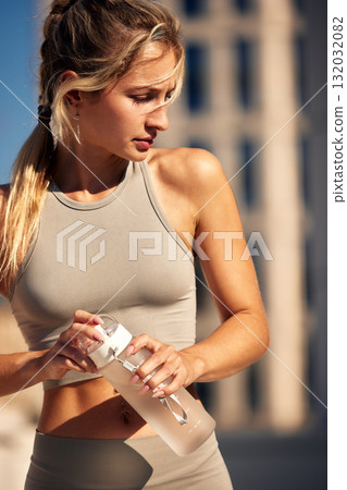 Healthy fitness model wearing beige sportswear outdoors, holding a water bottle during workout 132032082