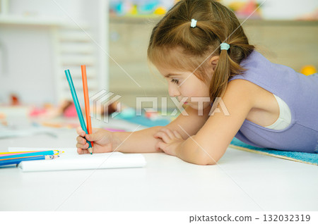 A girl is happily drawing with colorful pencils on the floor of her cheerful playroom 132032319
