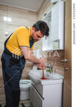 Plumber unclogging sink drain with plunger in bathroom 132032949