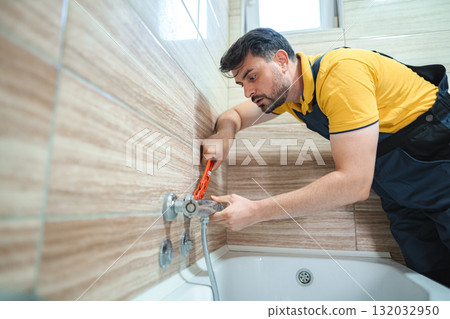 Plumber repairing faucet in bathroom using pipe wrench 132032950