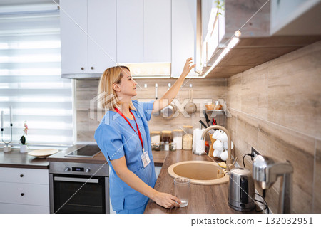 Nurse opening kitchen cabinet while holding glass of water 132032951