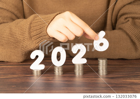 2026 New year saving money and financial planning concept. Female hands putting white number 2026 on stack of coins. Creative idea for business growth, tax payment, investment and banking. 132033076