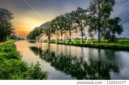 A Beautiful Serene Sunset Over a Tranquil Riverbank Surrounded by Lush Greenery and Nature A Beautiful Serene Sunset Over a Tranquil Riverbank Surrounded by Lush Greenery and Nature 132033277