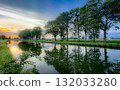 A Serene Sunset Reflection Along a Beautiful Tranquil Canal Surrounded by Lush Trees 132033280