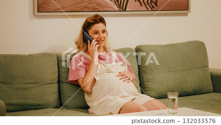 Portrait of smiling pregnant woman talking on smartphone on couch. 132033576