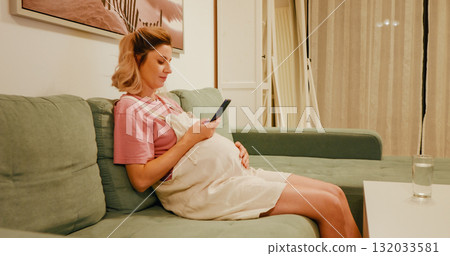 Expectant mom sitting on couch scrolling media. Expectant mom sitting on couch scrolling media. 132033581