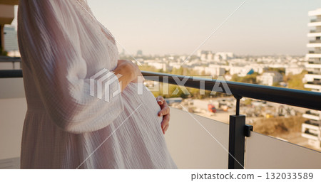 Pregnant Woman standing on the balcony and touching her big belly with love 132033589
