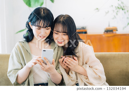 Two smiling women looking at a smartphone in a room 132034194