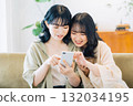 Two smiling women looking at a smartphone in a room 132034195