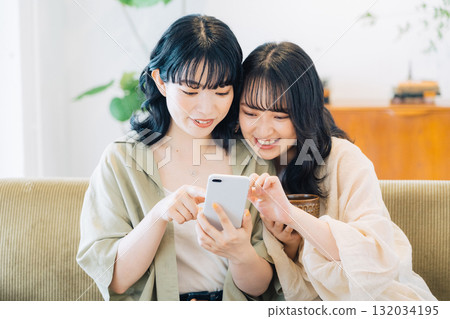 Two smiling women looking at a smartphone in a room 132034195