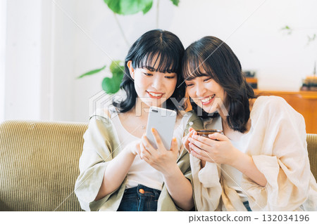 房間裡兩位面帶微笑的女人正在看智慧型手機 132034196