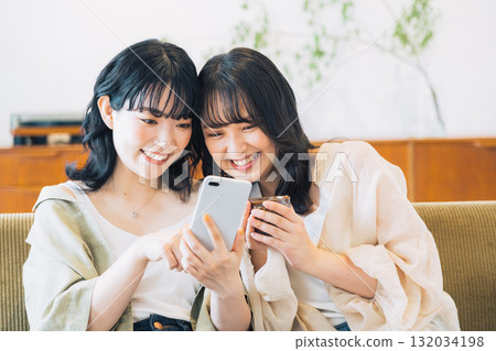 Two smiling women looking at a smartphone in a room 132034198