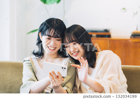 Two smiling women looking at a smartphone in a room 132034199