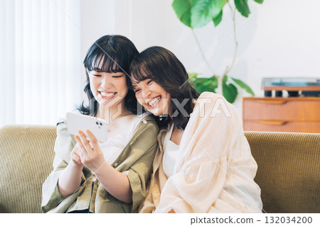 房間裡兩位面帶微笑的女人正在看智慧型手機 132034200