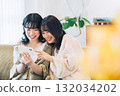 Two smiling women looking at a smartphone in a room 132034202