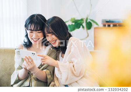 Two smiling women looking at a smartphone in a room 132034202