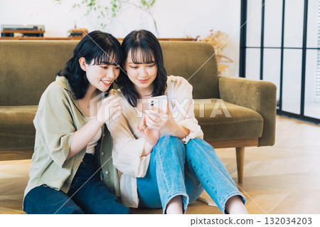 房間裡兩位面帶微笑的女人正在看智慧型手機 132034203