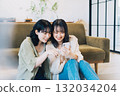 Two smiling women looking at a smartphone in a room 132034204