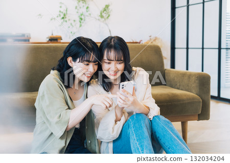 Two smiling women looking at a smartphone in a room 132034204