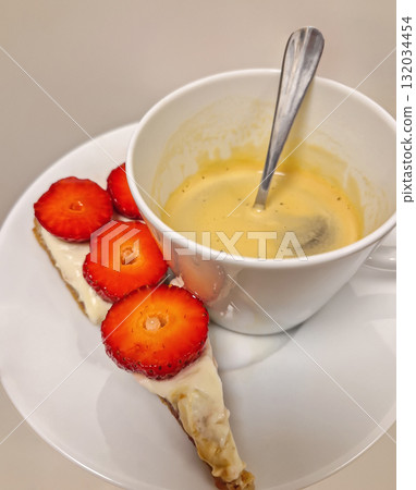 A cup of espresso with crema resting on a saucer with a slice of cake tart, topped with creamy white layer strawberries, creating an appetizing shot of a classic coffee and dessert pairing A cup of espresso with crema resting on a saucer with a slice of cake tart, topped with creamy white layer strawberries, creating an appetizing shot of a classic coffee and dessert pairing 132034454