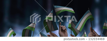 Uzbekistan flags in their hands on a blurred urban background 132034469
