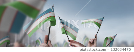 Uzbekistan flags in their hands on a blurred urban background 132034470