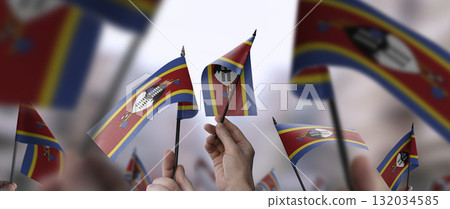 Swaziland flags in their hands on a blurred urban background Swaziland flags in their hands on a blurred urban background 132034585