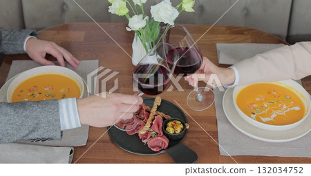 Couple having a dinner, clinking glasses of wine at a restaurant. People enjoying their date, drinking wine, eating and chatting. Couple having a dinner, clinking glasses of wine at a restaurant. People enjoying their date, drinking wine, eating and chatting. 132034752