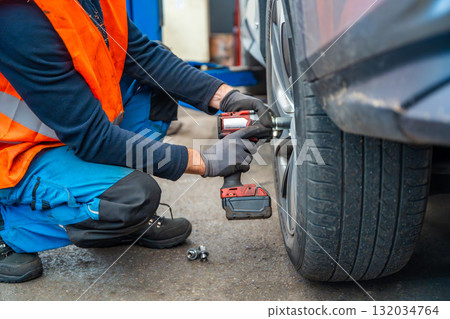 Mechanic using an impact wrench to remove lug nuts from a car wheel. Seasonal tire change and professional car service in preparation for winter. Mechanic using an impact wrench to remove lug nuts from a car wheel. Seasonal tire change and professional car service in preparation for winter. 132034764