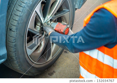 Mechanic using an impact wrench to remove lug nuts from a car wheel. Seasonal tire change and professional car service in preparation for winter. Mechanic using an impact wrench to remove lug nuts from a car wheel. Seasonal tire change and professional car service in preparation for winter. 132034767