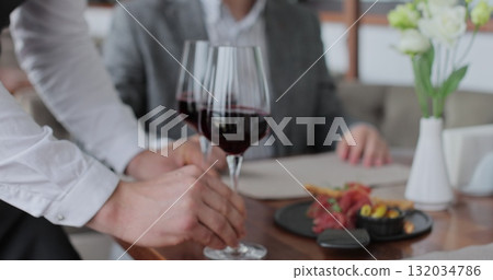 Waiter carries two glasses of wine to a young couple at a table in a restaurant. 132034786