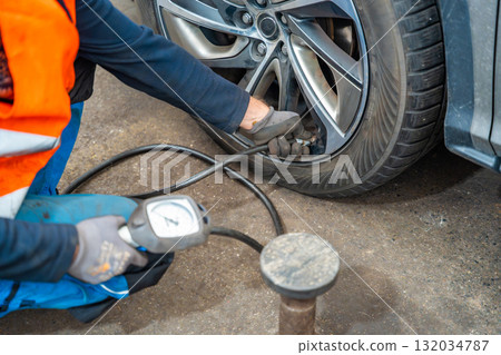 Worker checking tire pressure with gauge after seasonal wheel replacement. Final step of winter tire preparation in auto service in Czech Republic. Worker checking tire pressure with gauge after seasonal wheel replacement. Final step of winter tire preparation in auto service in Czech Republic. 132034787