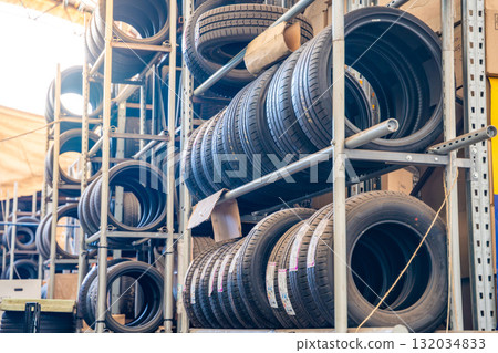 Multiple car tires and wheels stored in a large automotive workshop. Organized auto parts warehouse as part of seasonal tire service and maintenance. Multiple car tires and wheels stored in a large automotive workshop. Organized auto parts warehouse as part of seasonal tire service and maintenance. 132034833