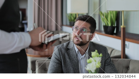 Waiter talking to man sitting at table placing order in restaurant. Waiter takes an order on a tablet. 132034844