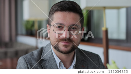Portrait of a bearded man with glasses in a cafe. Man sitting at the table looking at the camera and smiling. Happy man, customer and breakfast in restaurant, enjoy. Portrait of a bearded man with glasses in a cafe. Man sitting at the table looking at the camera and smiling. Happy man, customer and breakfast in restaurant, enjoy. 132034853