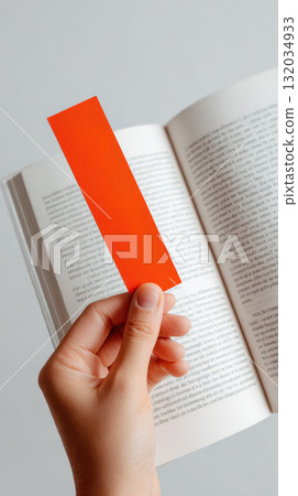 Hand holding orange bookmark open book reading study education vertical close up focus Hand holding orange bookmark open book reading study education vertical close up focus 132034933