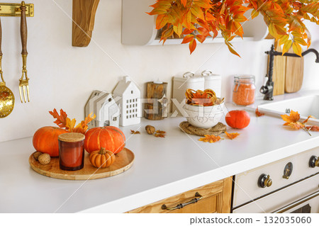 Autumn kitchen decor with pumpkins, cutting boards, and vibrant foliage in a bright space 132035060