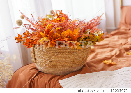 Autumn colored orange floral arrangement in woven basket placed on bed with soft linens, home decor Autumn colored orange floral arrangement in woven basket placed on bed with soft linens, home decor 132035071