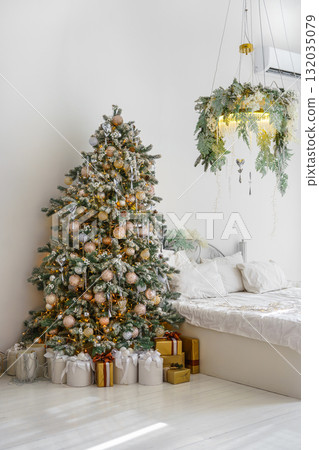 Holiday morning in bright, decorated room with Christmas tree and wrapped presents gathered by bed 132035079