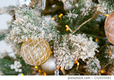 Frosted branches of Christmas tree with decorative gold and silver ornaments and shining lights 132035081