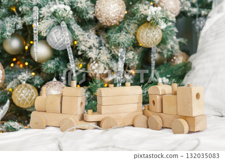 Wooden toy train with festive gift boxes on front of decorated Christmas tree in holiday interior 132035083