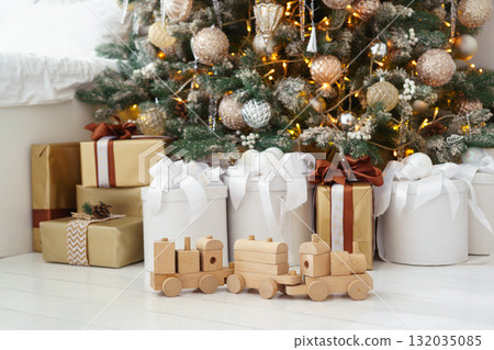 Wooden toy train with festive gift boxes under decorated Christmas tree in holiday interior Wooden toy train with festive gift boxes under decorated Christmas tree in holiday interior 132035085