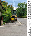 Two yellow road rollers parked on the street. Large and small yellow road rollers parked by the roadside near green trees. Construction machinery and heavy equipment outdoors. 132035807