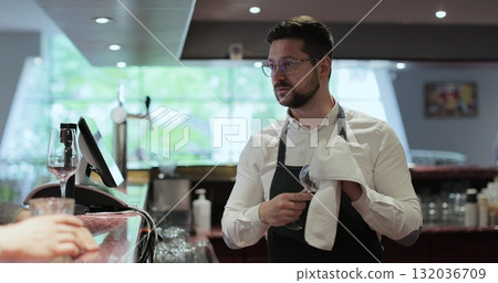 Barman wipes clear wineglass in restaurant. Hospitality industry, happy barista and wipe glassware for disinfection. Bar and cafe concept. Barman wipes clear wineglass in restaurant. Hospitality industry, happy barista and wipe glassware for disinfection. Bar and cafe concept. 132036709
