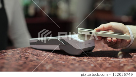 Purchase by smartphone on card reader. Pos-terminal in hand of waiter worker close-up. Modern technologies and restaurant business concept. 132036749
