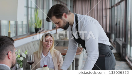 Waiter and coffee on a tray, walking to a customer in or restaurant cafe. Man and woman talking together and enjoying evening. 132036853