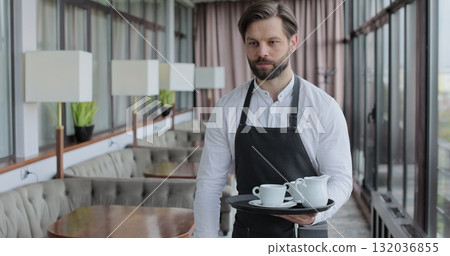 Waiter and coffee on a tray, walking to a customer in or restaurant cafe. Man and woman talking together and enjoying evening. 132036855